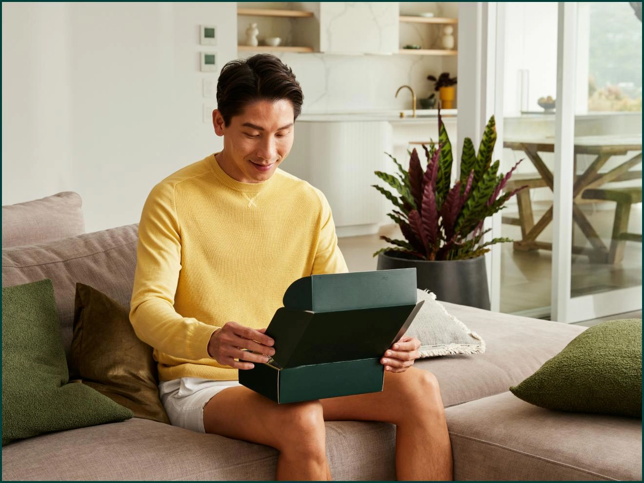 Man in a yellow sweater opening a Mosh box on the sofa